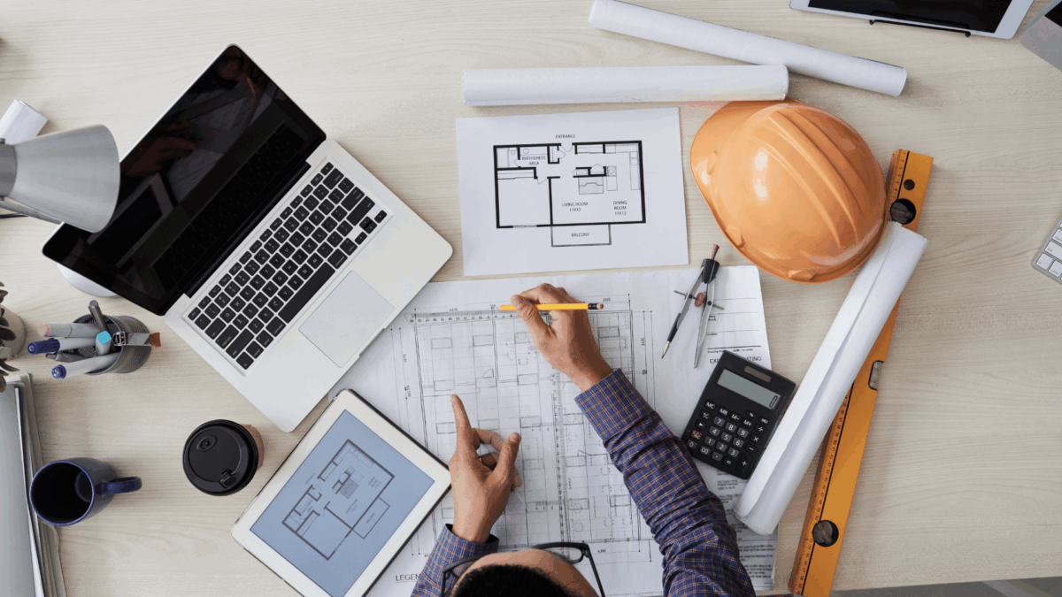 Design Engineering & Inspections Engineer writing on building plans with tools nearby.