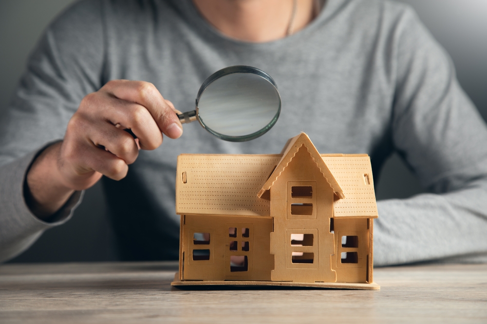 man holding a mangifying glass to inspect a house