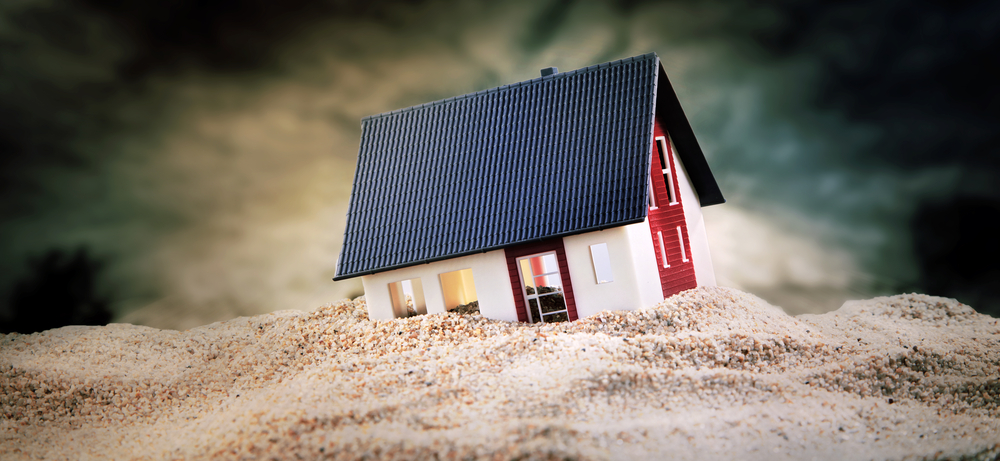 Small model home pictures sinking into sand foundation.