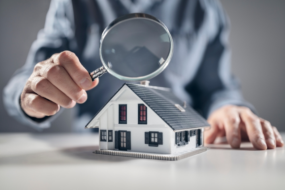 Small model home with structural engineer examining it with a magnifying glass. 